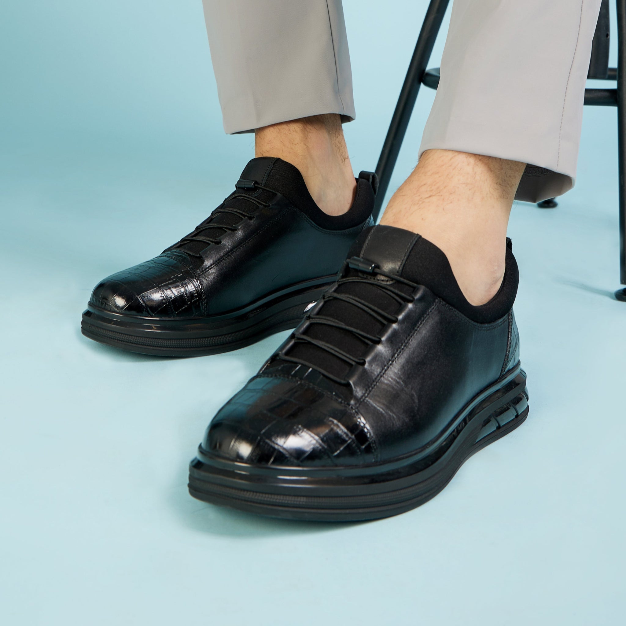 Person wearing black leather shoes and light gray pants on a light blue background