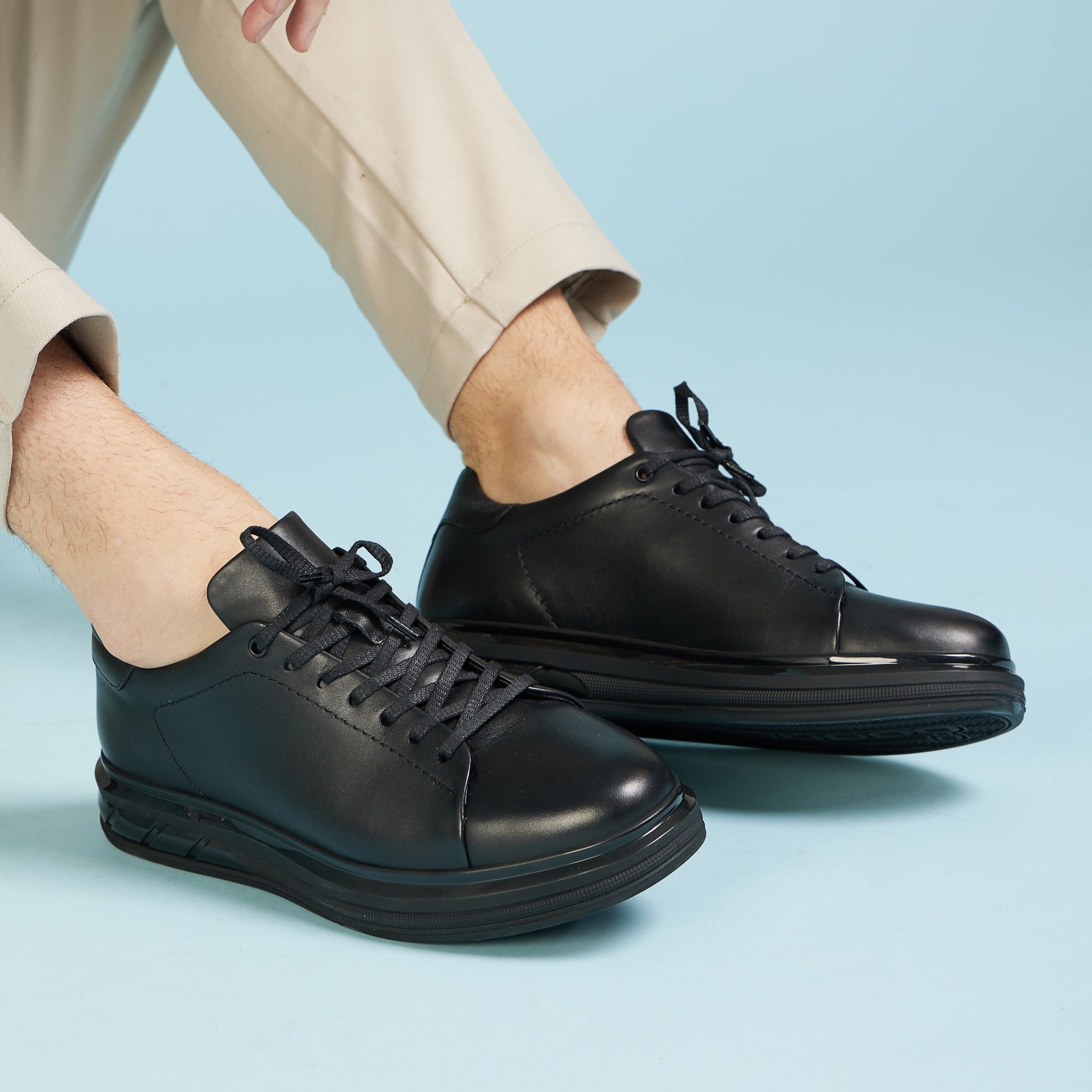 Person wearing black leather shoes on a light blue background